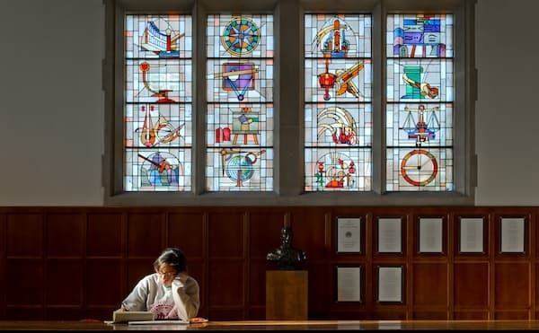 Student studying in the Great Hall of O'Shaughnessy under stained glass windows depicting the seven liberal arts.