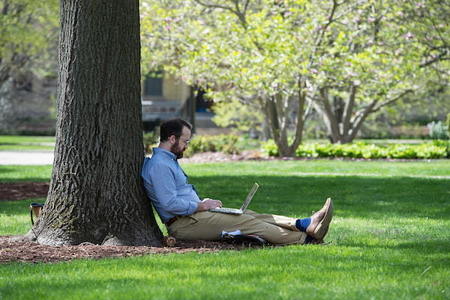 Student working on laptop outside under a tree in spring.